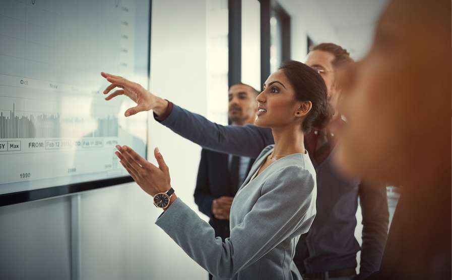 A group of business people pointing at a graph on a screen.