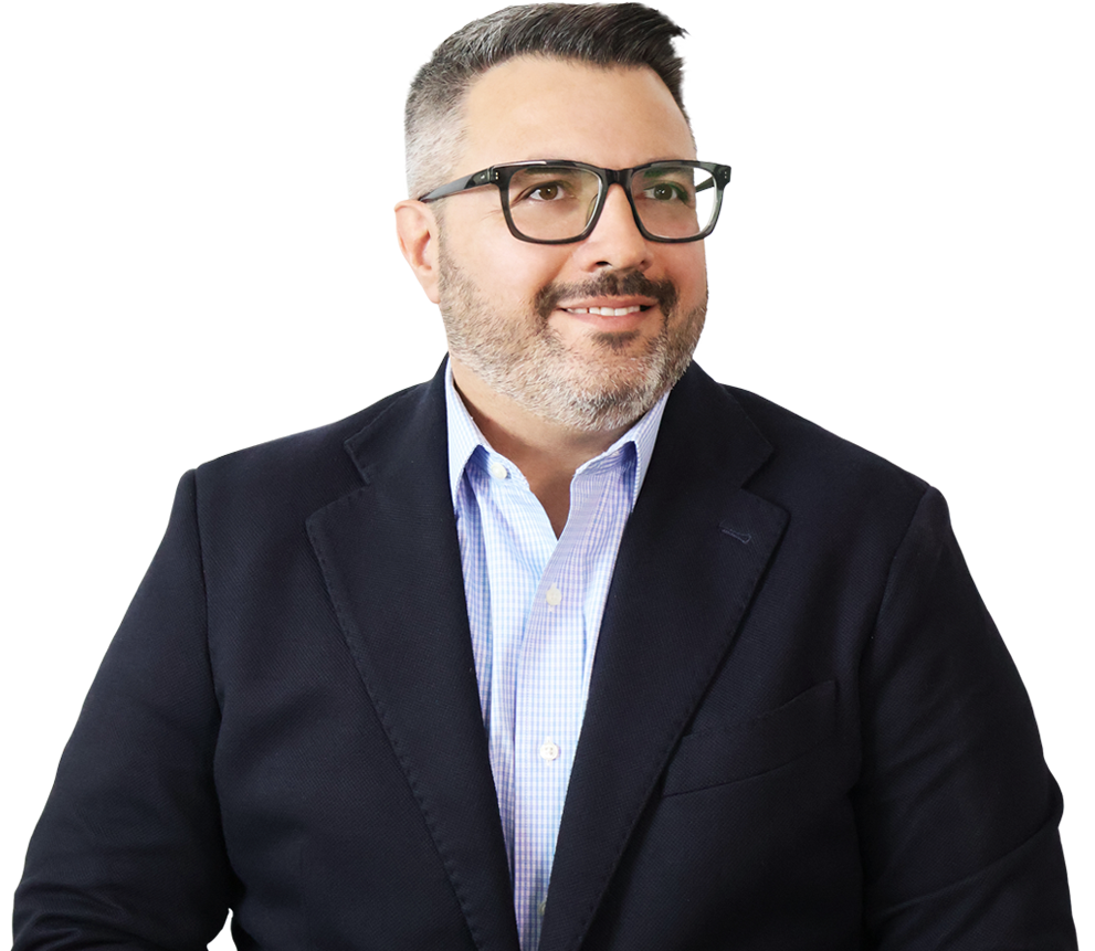 A man with short dark hair, glasses, and a beard is wearing a navy blazer over a light blue shirt, looking slightly to the left and smiling.
