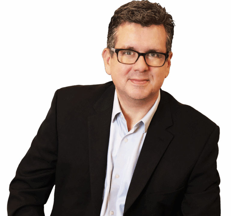 A man wearing glasses and a dark blazer over a light shirt sits and smiles at the camera against a white background.