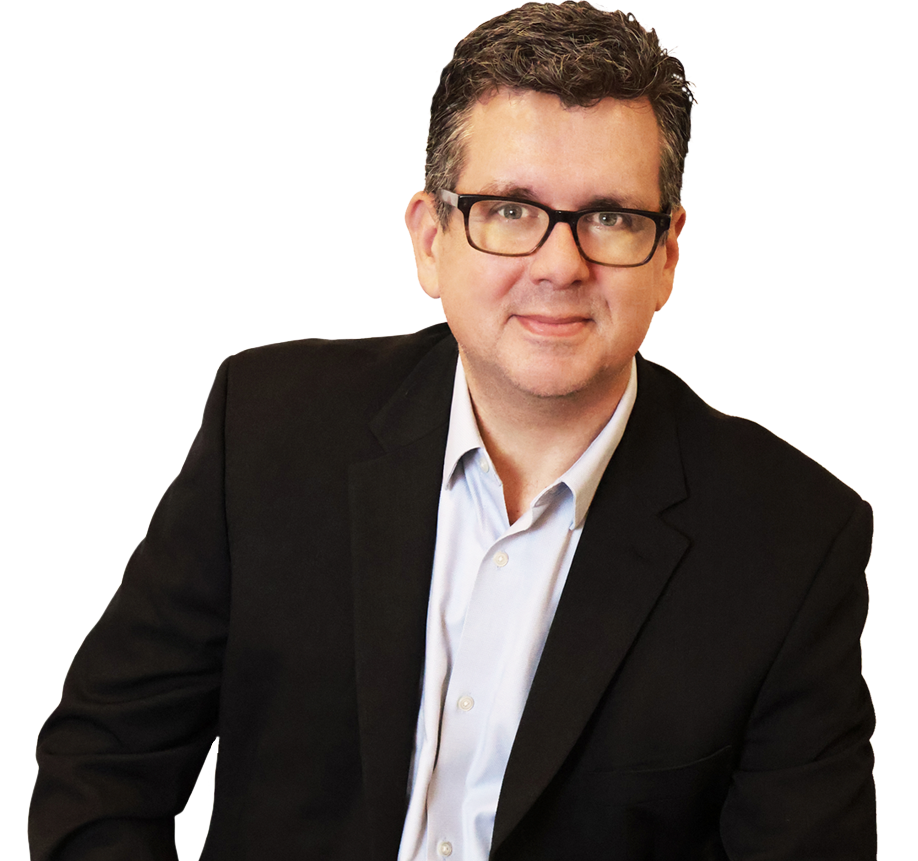 A man wearing glasses and a dark blazer over a light shirt sits and smiles at the camera against a white background.
