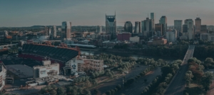 Aerial view of a city skyline with a football stadium in the foreground, surrounded by trees and a river.