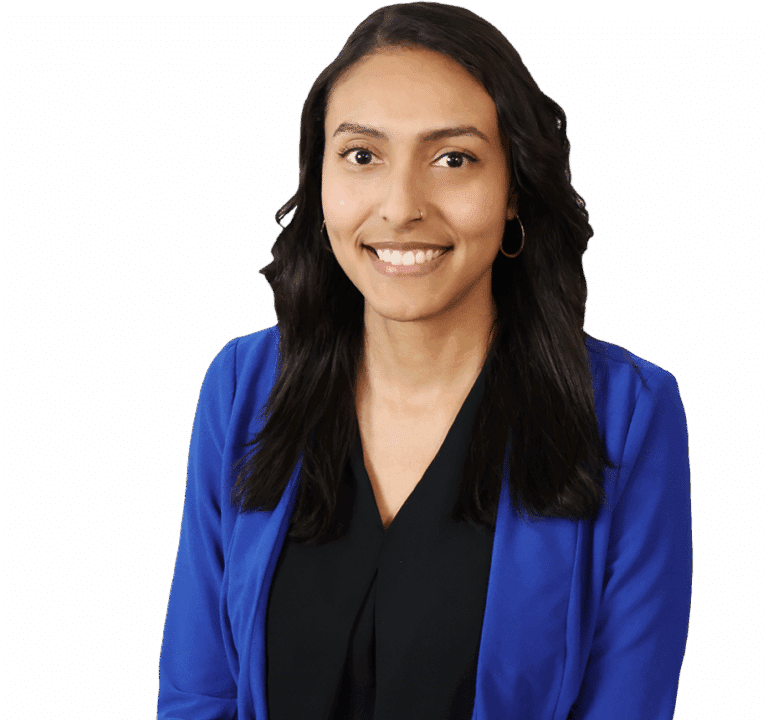 A woman with long dark hair, wearing a blue blazer and black top, sits and smiles at the camera against a white background.
