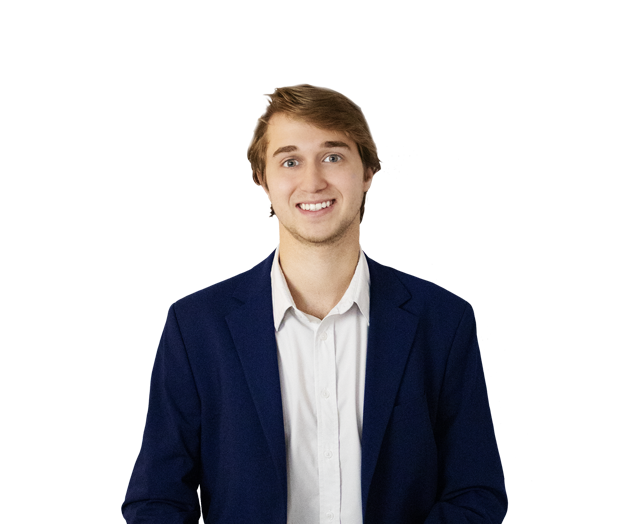 A young man with light brown hair, wearing a white shirt and dark blue blazer, smiling and standing against a plain white background.
