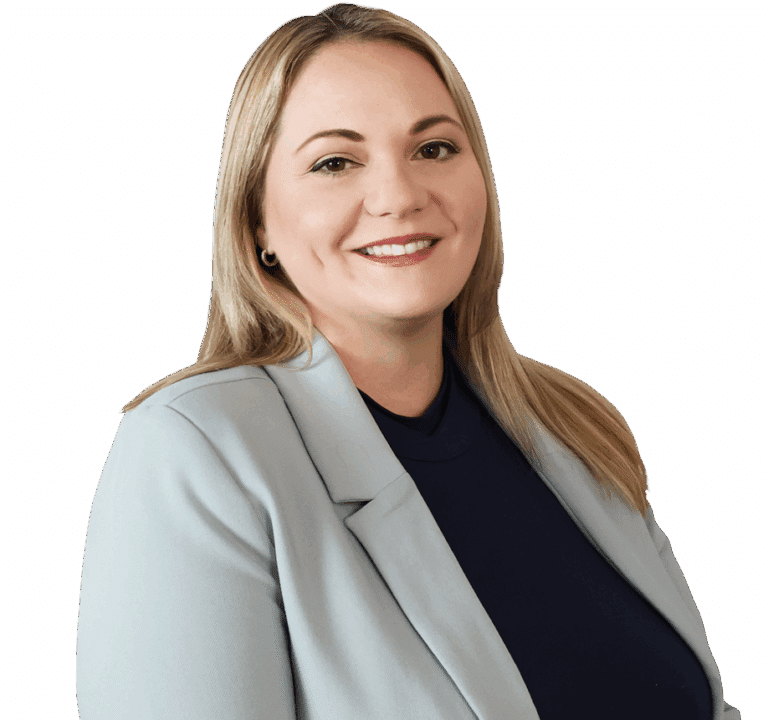 A woman with long blonde hair, wearing a light gray blazer over a dark top, smiles at the camera against a white background.