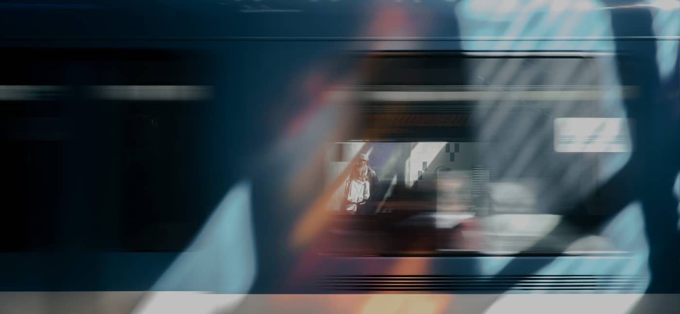 A person is visible through the window of a moving train, with reflections and motion blur creating abstract patterns across the image.