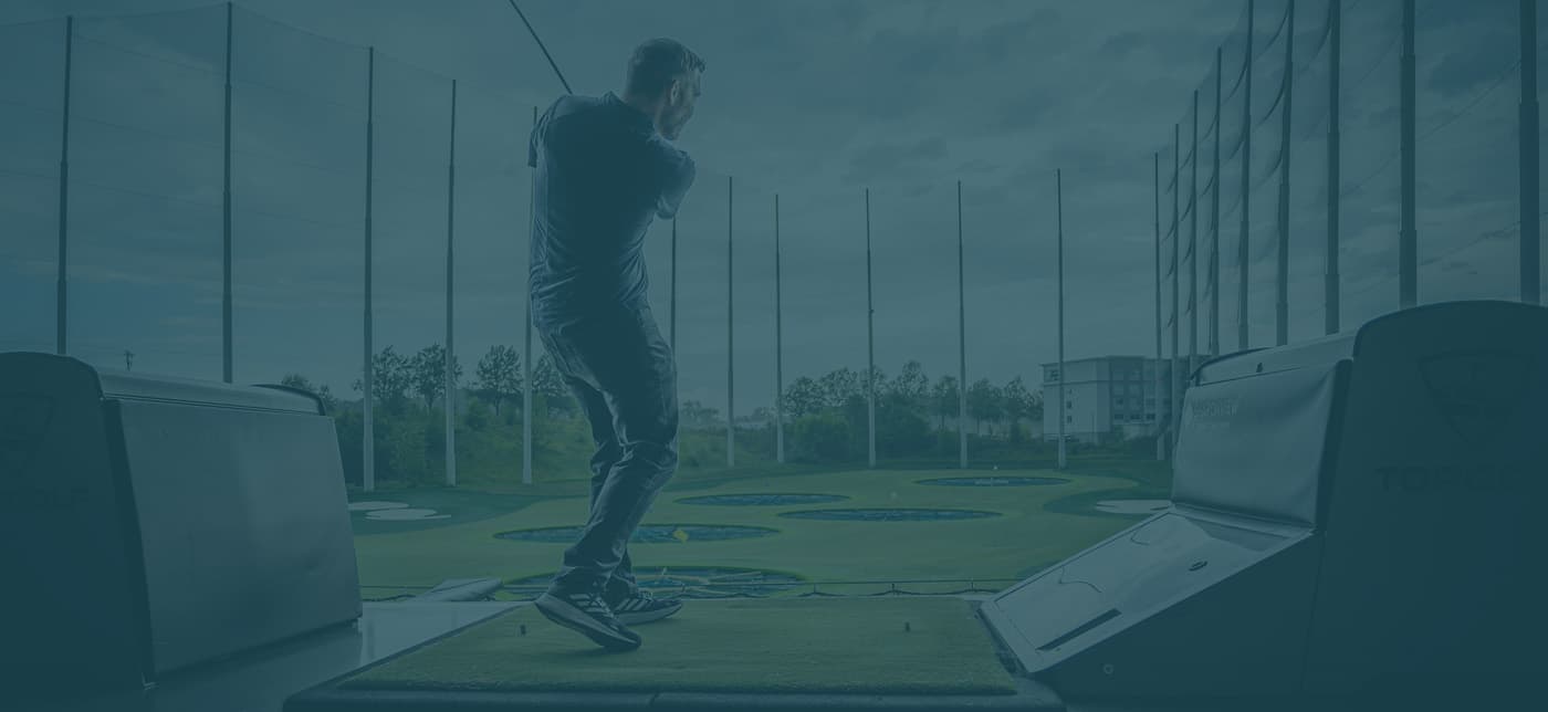 A person swings a golf club at an indoor driving range with multiple targets visible on the green outside.
