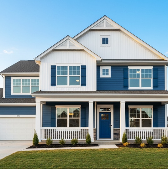 Two-story modern suburban house with blue siding, white trim, a covered front porch, and a neatly manicured lawn under a clear blue sky.