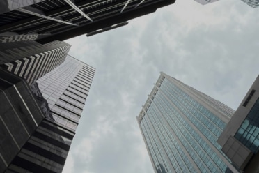 Skyscrapers viewed from below against a cloudy sky, showing modern glass and steel architecture.
