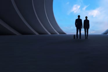 Two people in business attire stand inside a large, modern, curved structure, looking out at a blue sky with clouds through a wide opening.