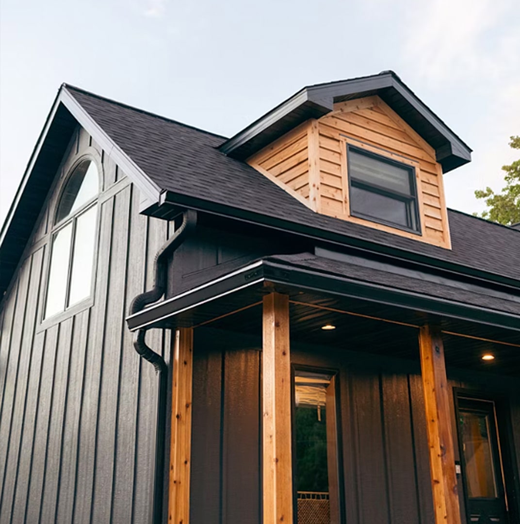 A modern house with dark vertical siding, wooden trim, and a dormer window on the roof.