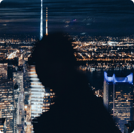 Silhouette of a person in front of a brightly lit city skyline at night.