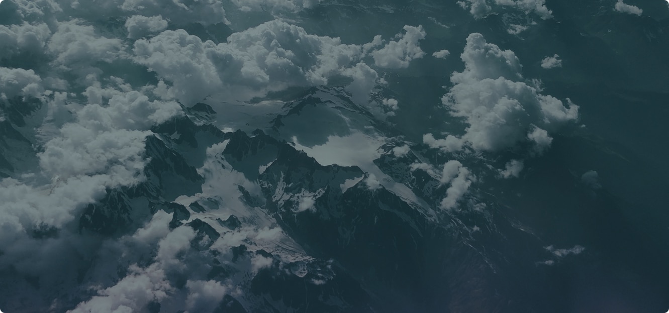 Aerial view of snow-covered mountain peaks partially obscured by dense clouds.