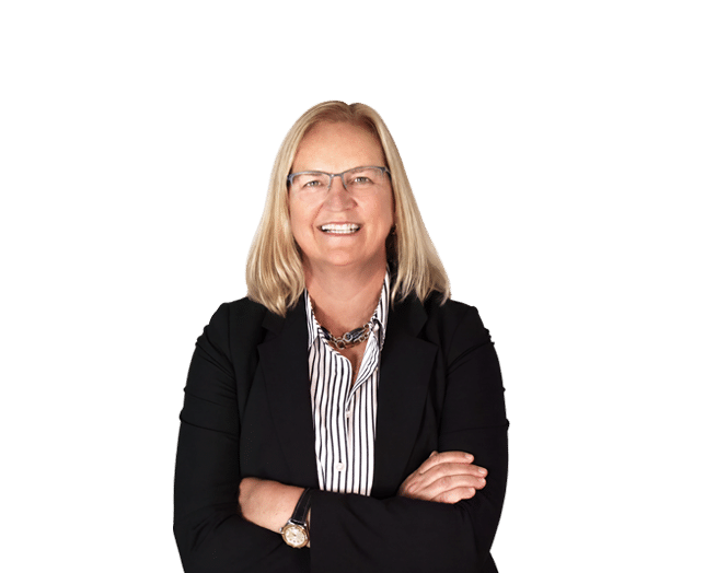 A woman with blonde hair and glasses, wearing a black blazer and striped shirt, stands smiling with arms crossed against a plain white background.