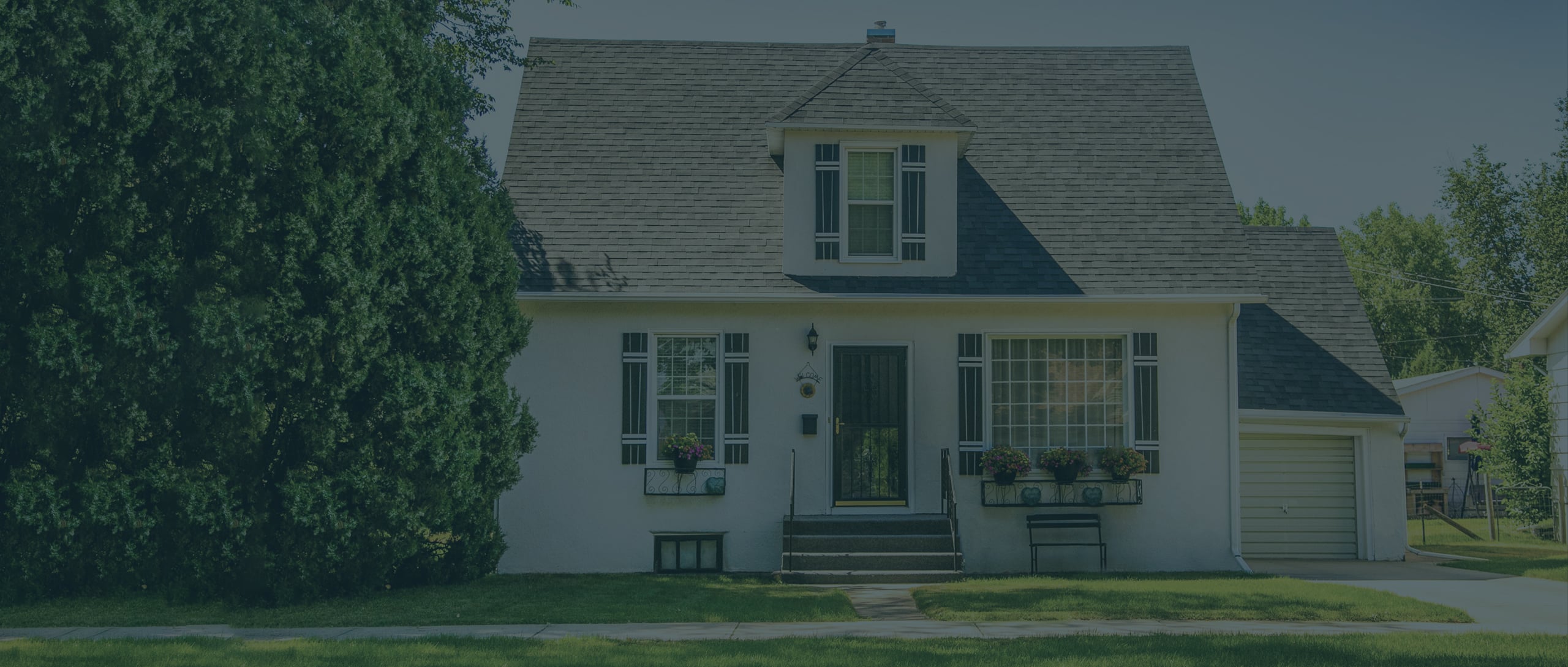 A white house with a steep roof, central front steps, shuttered windows, flower boxes, and an attached single-car garage.