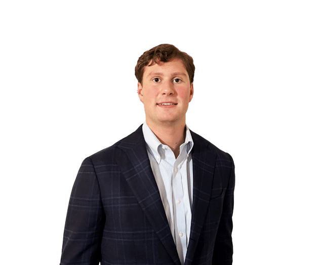 Man wearing a dark plaid blazer and a light striped shirt, standing against a plain white background, facing the camera with a slight smile.