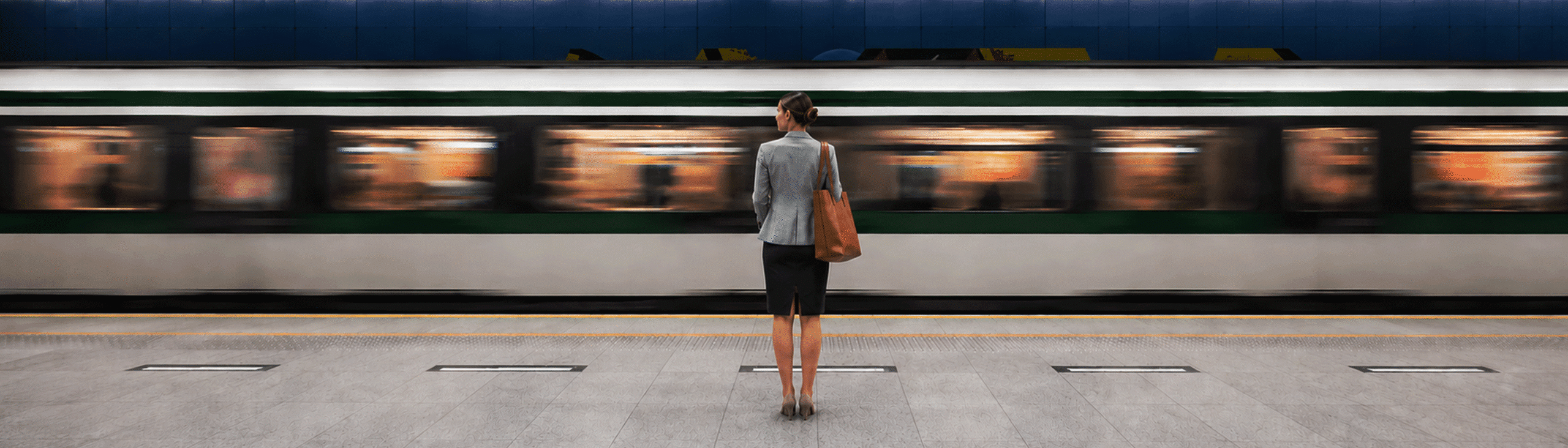 A woman stands on a train platform facing a moving train, with the station floor and blue-tiled wall visible in the background.