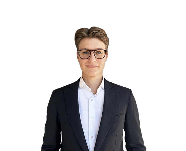 A young man wearing glasses, a white shirt, and a dark suit jacket stands against a plain white background, facing the camera.
