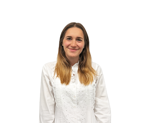 A young woman with long, light brown hair wearing a white blouse stands in front of a plain white background, smiling at the camera.