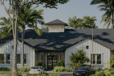 Single-story white house with a dark roof, surrounded by palm trees and greenery; two cars are parked in the driveway on a sunny day, capturing the charm and allure of Florida real estate.