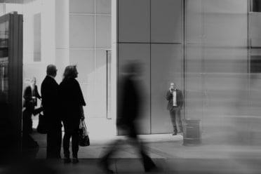 People walking in front of modern office buildings, some in focus and others blurred in motion. Urban street scene with business attire and a van passing by, capturing the energy of a city that thrives on financing through every stage of an investment.
