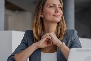 Woman in a gray blazer sits at a desk with a tablet, looking thoughtfully to the side in a modern office setting—perhaps considering how to prep your property for a smooth appraisal.